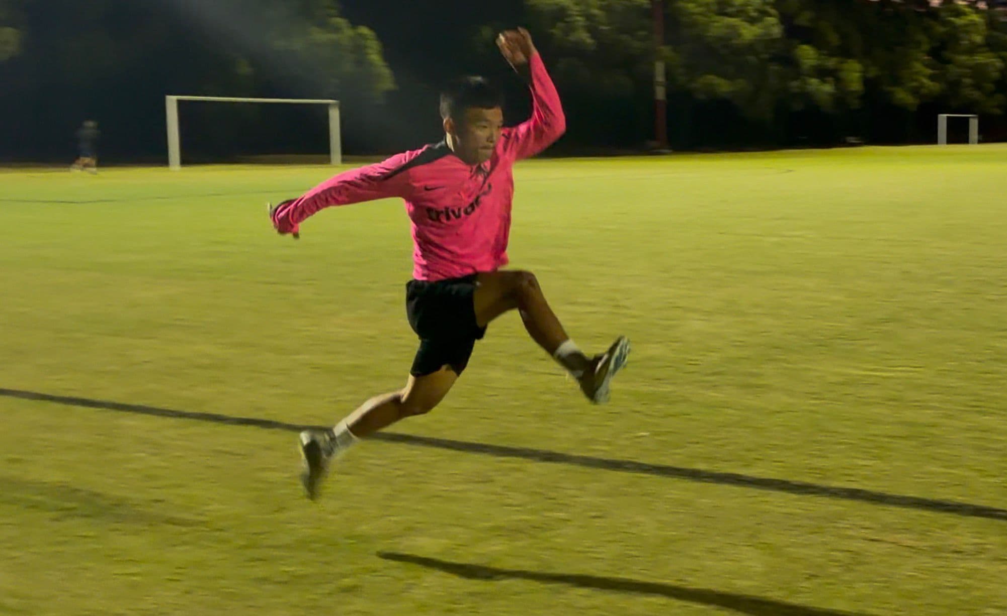 Athlete mid-flight in a horizontal bound under stadium lights, knee driven up, opposite arm in counter-balance, elastic energy releasing into horizontal projection